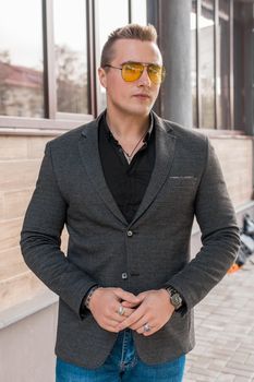 Stylish young guy portrait businessman of European appearance in a gray jacket and black shirt in sunglasses on the street outdoor.
