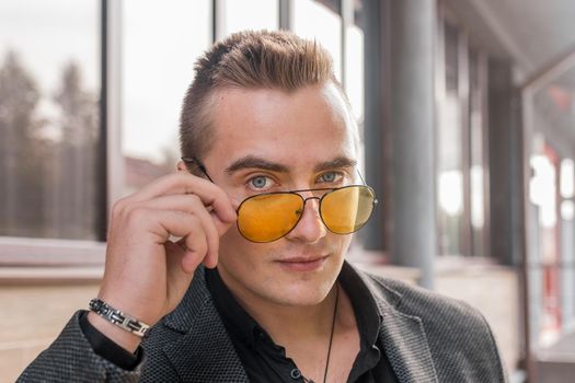 Portrait of a handsome man of European appearance businessman adjusting sunglasses with his hand, close-up on the outdoor of the street.