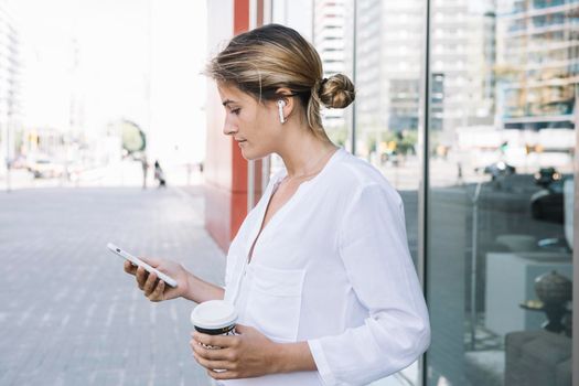 blonde young woman holding smart phone takeaway coffee cup hands