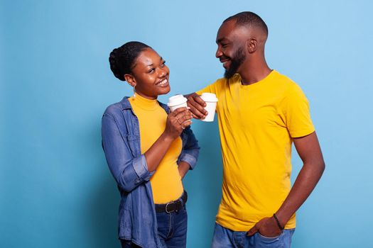 Cheerful couple holding cup of coffee and enjoying romance in front of camera. People in relationship laughing and looking at each other. Boyfriend and girlfriend showing affection.