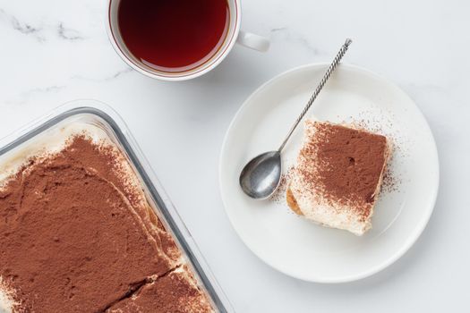 Piece of Homemade Tiramisu cake dessert and coffee on a white marble background