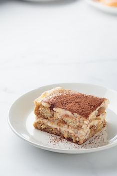 Piece of Homemade Tiramisu cake dessert on a white marble background