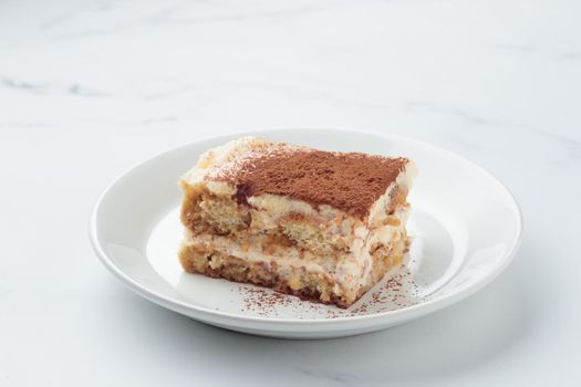 Piece of Homemade Tiramisu cake dessert on a white marble background