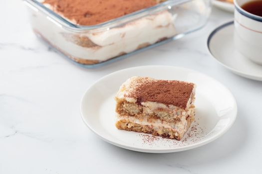 Piece of Homemade Tiramisu cake dessert on a white marble background