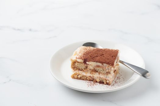 Piece of Homemade Tiramisu cake dessert on a white marble background