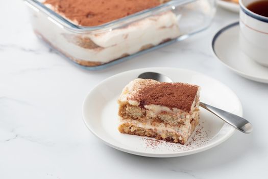 Piece of Homemade Tiramisu cake dessert on a white marble background