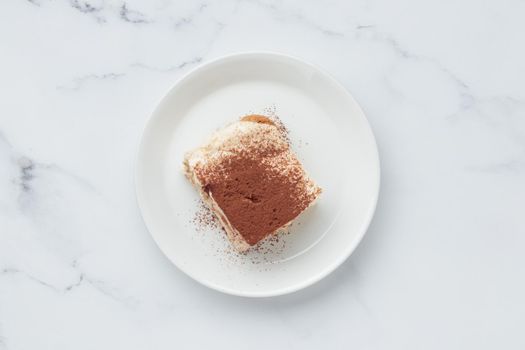 Piece of Homemade Tiramisu cake dessert on a white marble background