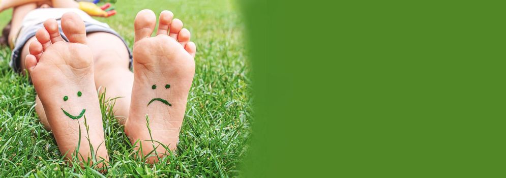 Baby feet with paint pattern are smiling and sad on the green grass. Selective focus. nature.
