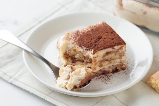 Piece of Homemade Tiramisu cake dessert with savoiardi as ingredients on a white marble background