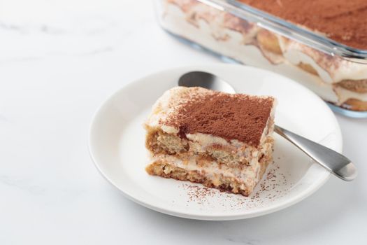 Piece of Homemade Tiramisu cake dessert with savoiardi as ingredients on a white marble background