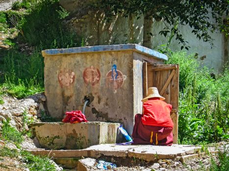 Tibetan monk in red tunic at work while washing clothes, travel reportage