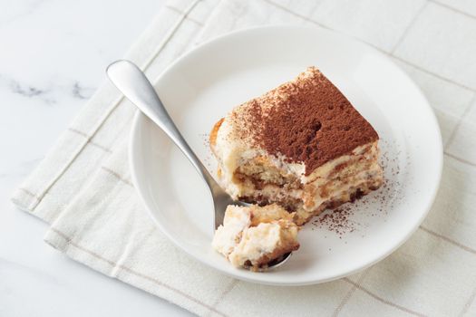 Piece of Homemade Tiramisu cake dessert on a white marble background