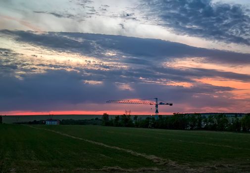 Landscape with building and silhouette of the crane in the field.
