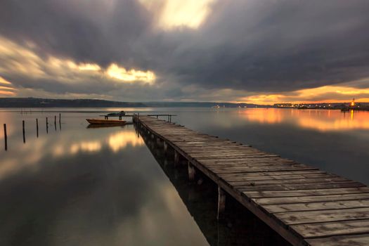 The long exposure view on a cloudy day on the lake with a boat at a wooden pier.