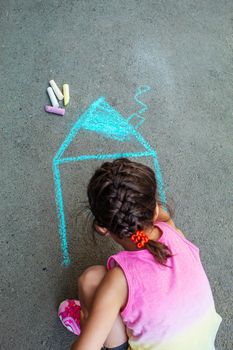 The child draws the house with chalk on the asphalt. Selective focus. draw.