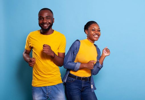 African american couple doing dance moves together in studio, feeling cheerful and carefree. Happy people dancing on rhythm and smiling in front of camera, having fun in relationship.