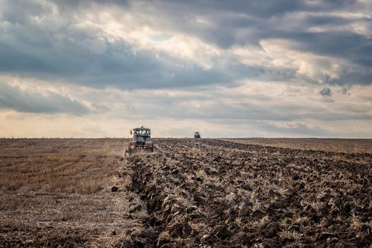 Day view of tractors plowing the soil in a mountain hill. Horizontal view