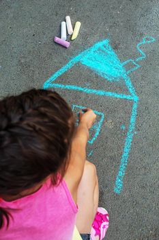 The child draws the house with chalk on the asphalt. Selective focus. draw.