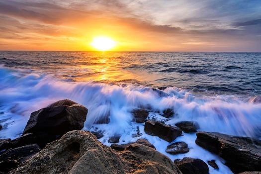 The stunning seascape with the colorful sky and water foam at the rocky coastline of the Black Sea