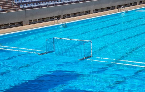 Empty water polo goal. Water sports equipment. Water polo goal with white frame and net supported with rope and floating buoys resting on the swimming pool.