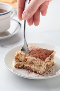 Piece of Homemade Tiramisu cake dessert on a white marble background