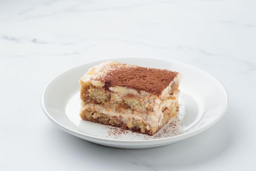 Piece of Homemade Tiramisu cake dessert on a white marble background