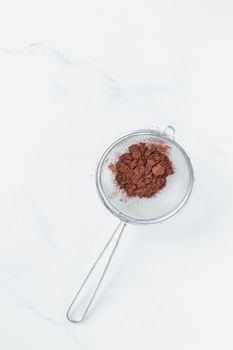 Cocoa powder sweet ingredient in a strainer on a white backround top view