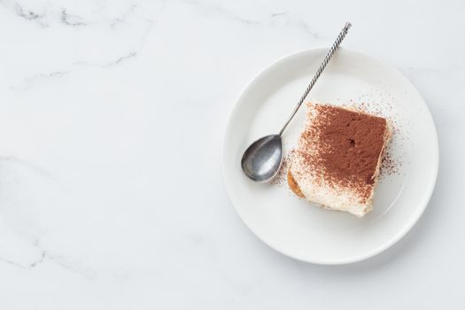 Piece of Homemade Tiramisu cake dessert on a white marble background