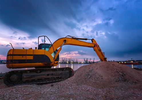 Crawler excavator during earthmoving works on construction site at sunset