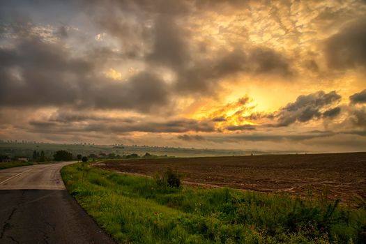 The landscape at the road through in the field with colorful clouds