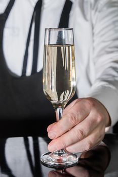 A professional bartender serves chilled champagne sparkling with gases in glass on the bar.