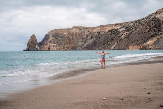 A plump woman in a bathing suit enters the water during the surf. Alone on the beach, Gray sky in the clouds, swimming in winter