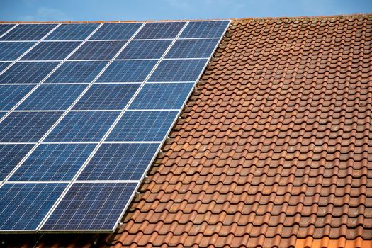 solar panels on roof of house. horizontal orientation, blue sky, gray panels on brown roof.