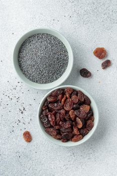 Bowls with poppy seeds and raisins on concrete background top view