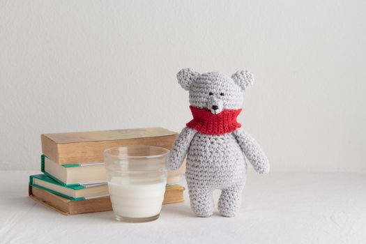 Crochet knitting cute teddy bear with books and a toy on a white table