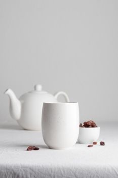 White teacup with raisins and teapot on a white background