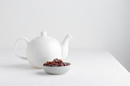 White teapot with raisins on a table on a white background