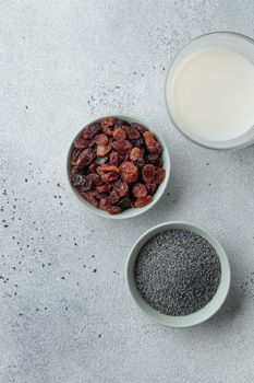Bowls with poppy seeds and raisins on concrete background top view