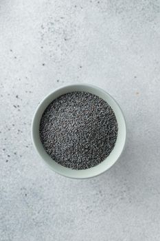Bowl with poppy seeds on concrete background top view