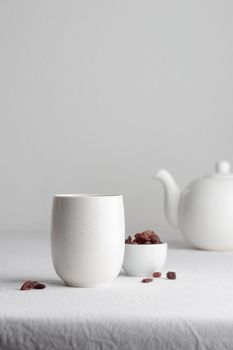 White teacup with raisins and teapot on a white background