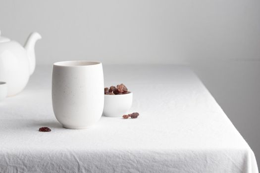 White teacup with raisins and teapot on a white background