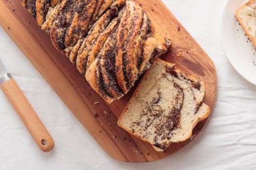 Piece of swirl homemade bread with poppy seeds on a white table