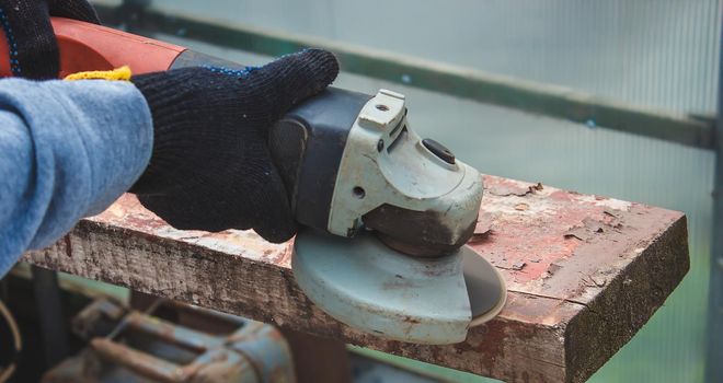 a man is grinding a board. Removing old paint from boards. Carpentry work. selective focus