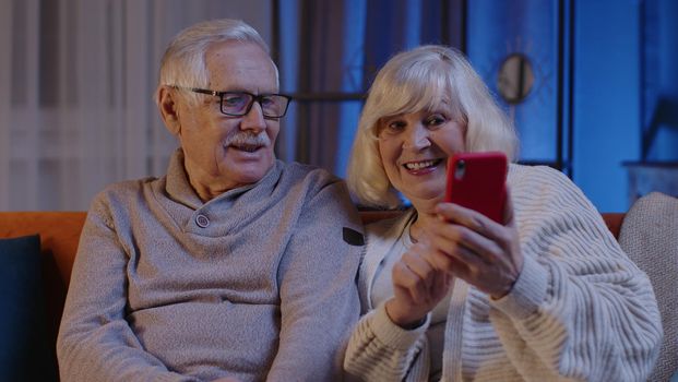 Mature Grandmother Grandfather Making Video Call Online On Mobile Phone At Home Sofa. Senior Old Couple Grandparents Having Conversation Webcam Chat. Happy Old Family Using Smartphone. 6k Downscale