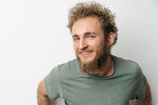 Young handsome with bright blue eyes bearded wild curly hair man isolated on white background. Young thinking man in green t-shirt on white background. Copy space.