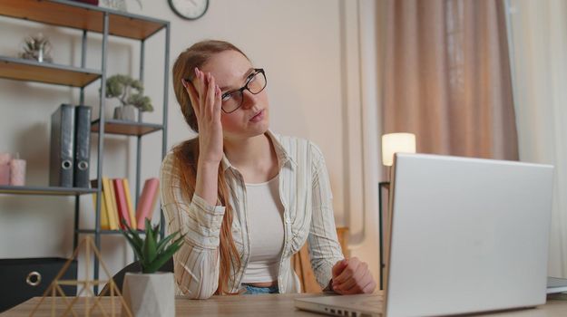 Tired woman freelancer teacher using laptop computer, suffering from tension, migaine headache after e-learning, remote working job with pupils sitting at home office table. Adult girl businesswoman