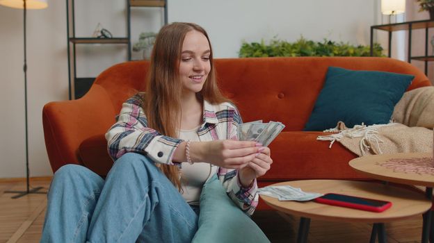 Planning family budget. Smiling happy young woman counting money cash, calculate domestic bills at home. Joyful girl satisfied of income and saves money for a planned vacation, gifts, future expenses