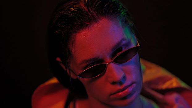 Portrait of young woman wearing jacket and sunglasses in neon color lights . Pretty girl in neon light on black background. Night club, Party concept.