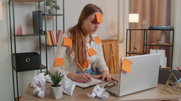 Exhausted woman freelancer with pasted sticker notes using laptop computer having concentration problem, creative crisis. Nervous adult girl confused by big routine work loading indoors at home office