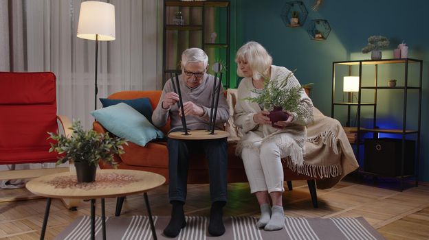 Senior old couple grandfather, grandmother finishing assembling furniture at home. Successful table collect, repair, fixing. Elderly family man woman after moving into new apartment. Mortgage concept